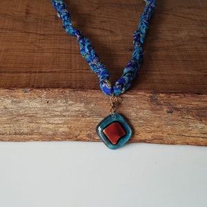 May include: A blue and white fabric necklace with a blue and orange glass pendant.