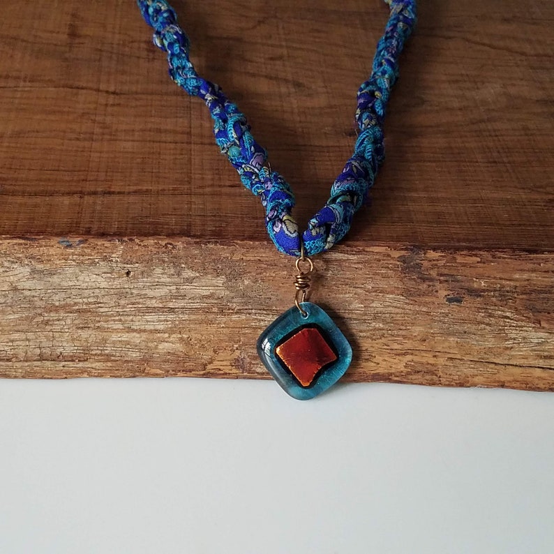 May include: A blue and white fabric necklace with a blue and orange glass pendant.