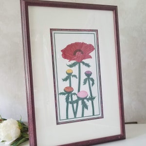 May include: Framed print of a red poppy flower with five buds in shades of pink, yellow, and red. The flowers are depicted in a stylized, almost graphic, manner against a white background.