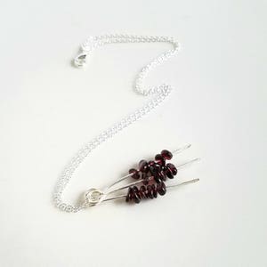 May include: A silver chain necklace with a pendant made of three silver wires with small, dark red garnet stones attached.
