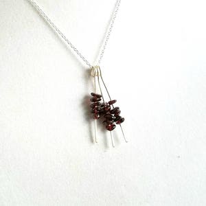May include: A silver chain necklace with a pendant made of multiple thin silver wires with small, dark red garnet beads clustered at the bottom.