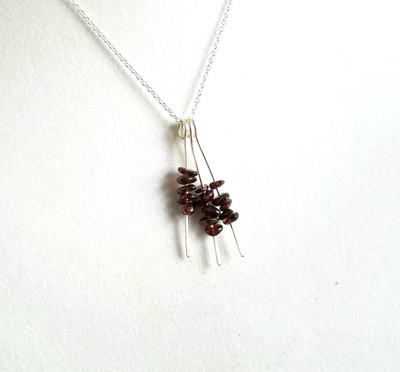 May include: A silver chain necklace with a pendant made of multiple thin silver wires with small, dark red garnet beads clustered at the bottom.