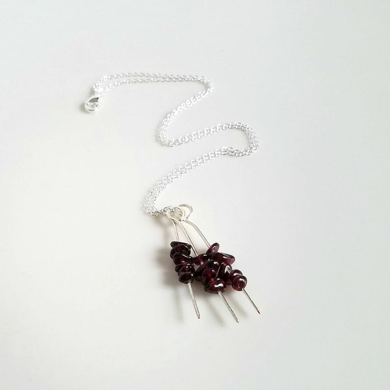 May include: A silver chain necklace with a pendant featuring a cluster of dark red garnet stones on three silver wires.