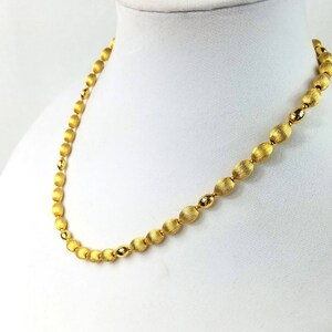 Op de afbeelding: Een gouden ketting met ovale kralen. De kralen hebben een getextureerd oppervlak.