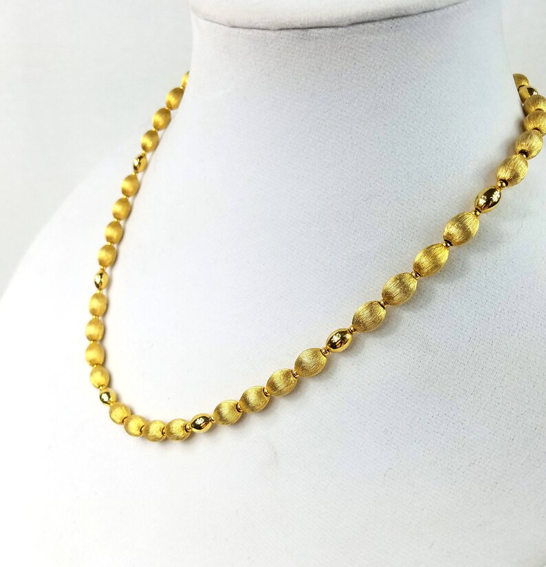 Op de afbeelding: Een gouden ketting met ovale kralen. De kralen hebben een getextureerd oppervlak.