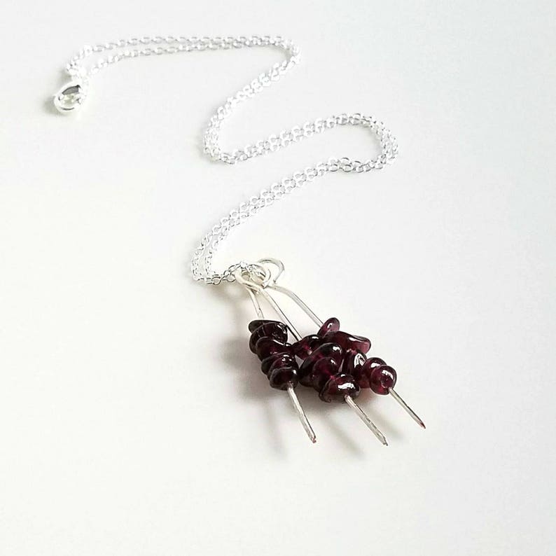 May include: A silver chain necklace with a pendant featuring a cluster of dark red garnet stones on three silver wires.
