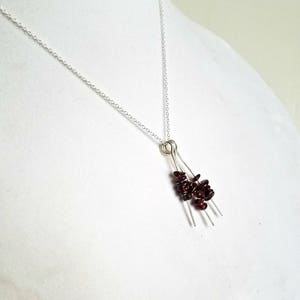 May include: A silver chain necklace with a pendant featuring a cluster of small, dark red garnet stones hanging from three silver wires.