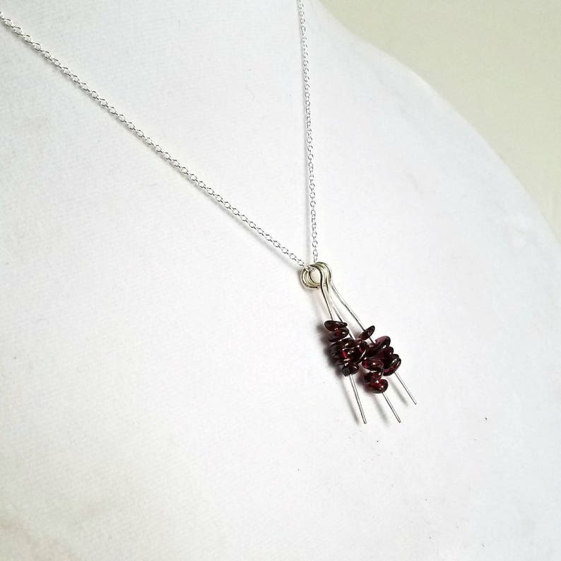 May include: A silver chain necklace with a pendant featuring a cluster of small, dark red garnet stones hanging from three silver wires.