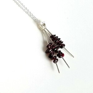 May include: A silver necklace with a pendant featuring three strands of dark red garnet beads.