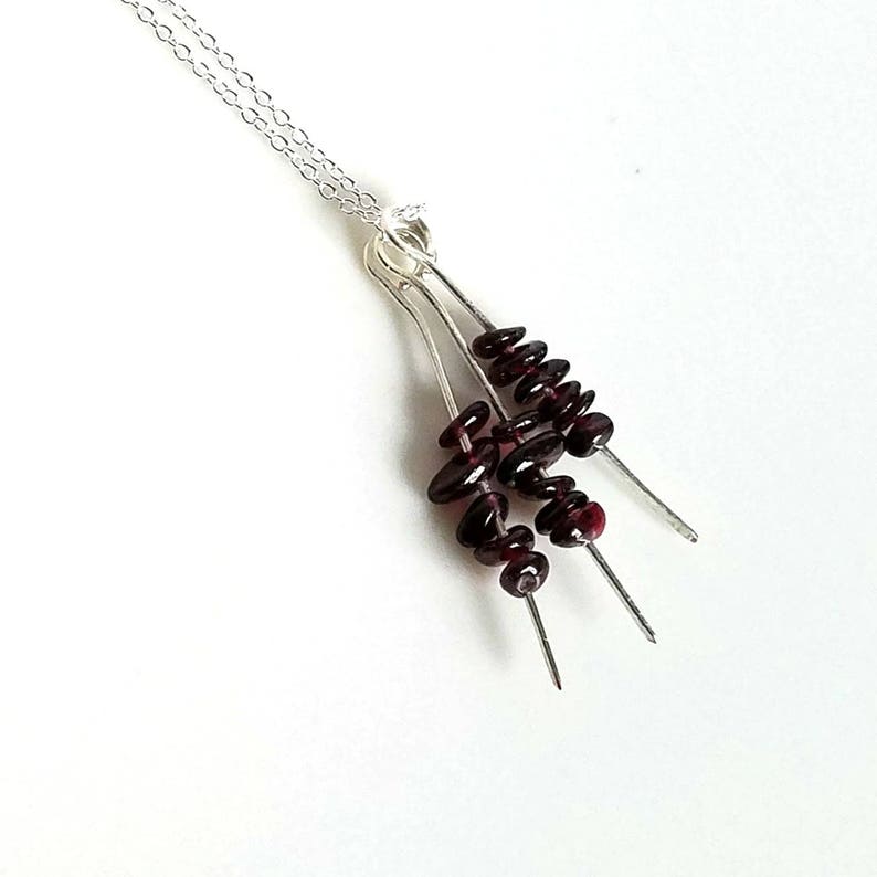 May include: A silver necklace with a pendant featuring three strands of dark red garnet beads.