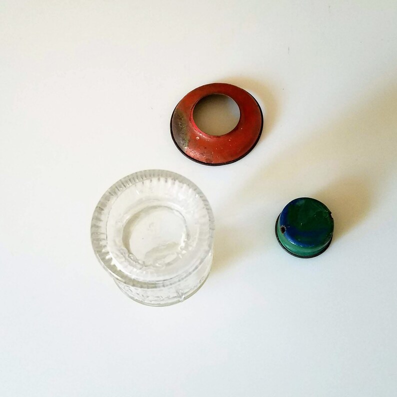 Puede incluir: Tres tapas de tarro de vidrio, una con tapa de metal roja, otra con tapa de metal verde y azul, y otra con tapa de vidrio transparente.