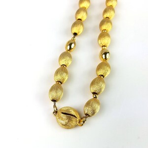 Op de afbeelding: Een gouden ketting met ovale kralen. De kralen hebben een getextureerde, geborstelde afwerking.