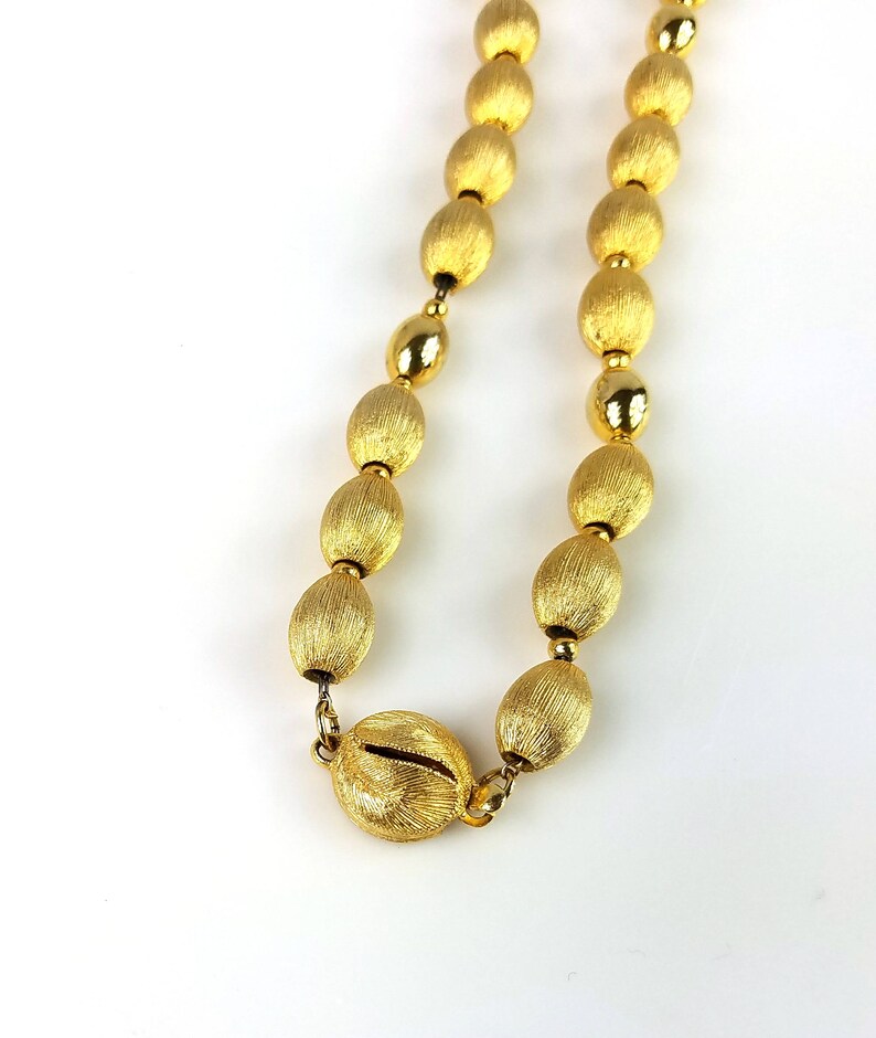 Op de afbeelding: Een gouden ketting met ovale kralen. De kralen hebben een getextureerde, geborstelde afwerking.