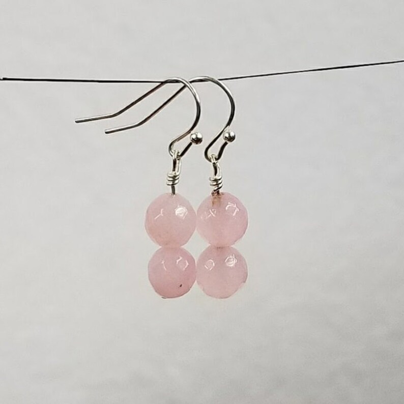 May include: A pair of silver dangle earrings with two pink round beads on each earring.