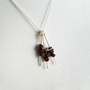 May include: A silver chain necklace with a pendant featuring multiple strands of small, dark red garnet stones.