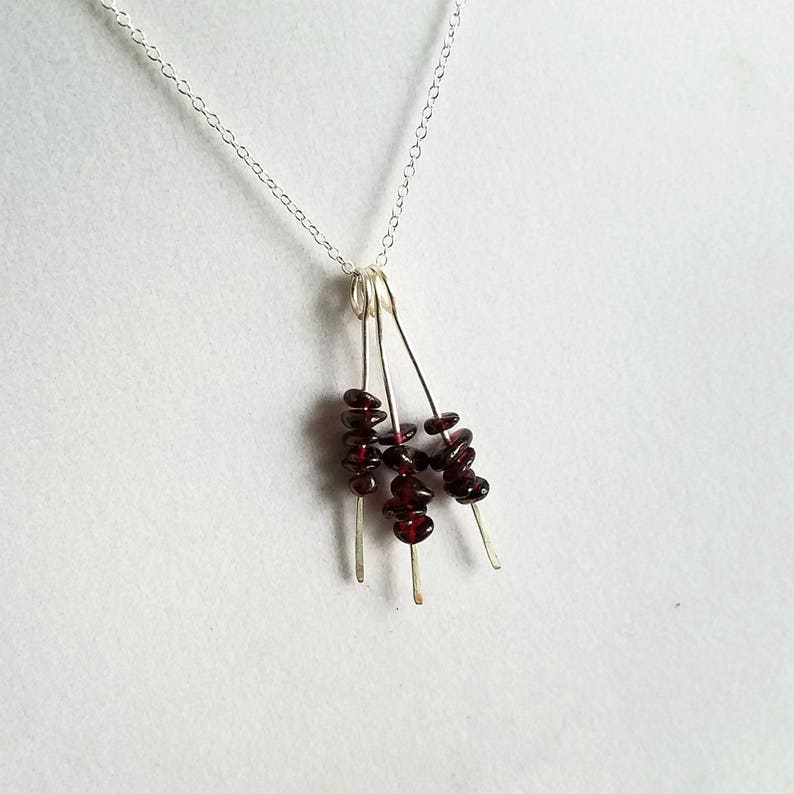 May include: A silver chain necklace with a pendant featuring multiple strands of small, dark red garnet stones.
