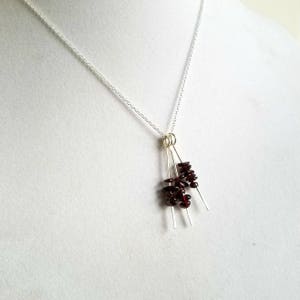 May include: A silver chain necklace with a pendant made of three silver wires with clusters of small, dark red garnet stones attached.