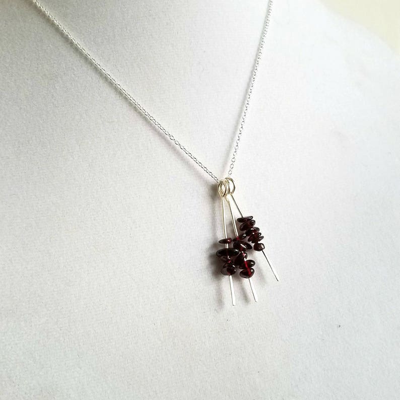 May include: A silver chain necklace with a pendant made of three silver wires with clusters of small, dark red garnet stones attached.