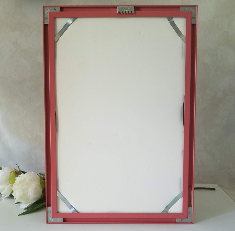 May include: A coral pink picture frame with a white mat and silver metal hanging hardware. The frame is empty.