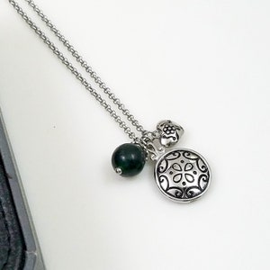 May include: A silver chain necklace with three charms: a green bead, a heart charm with a floral design, and a round charm with a decorative pattern.