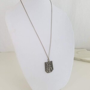 May include: A silver chain necklace with a silver pendant featuring a detailed design of a person standing in a doorway.