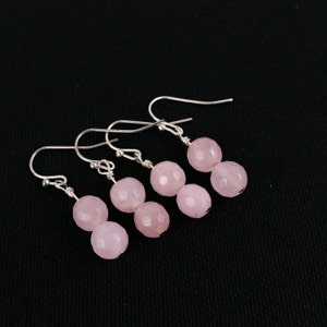 May include: A pair of silver earrings with two pink faceted gemstone beads on each earring.