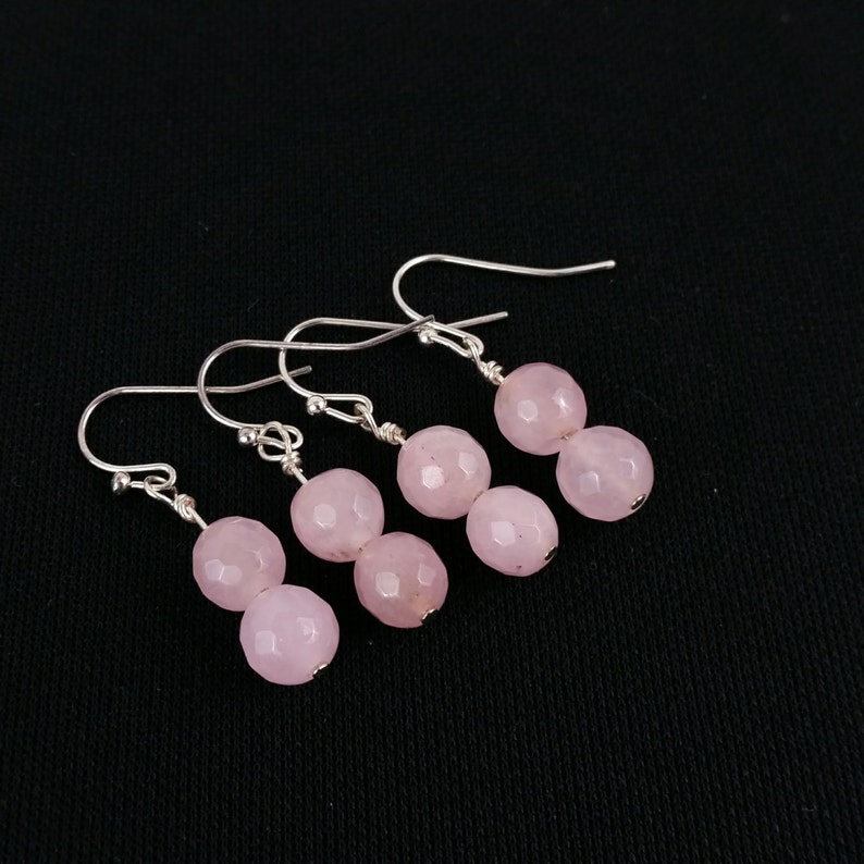 May include: A pair of silver earrings with two pink faceted gemstone beads on each earring.