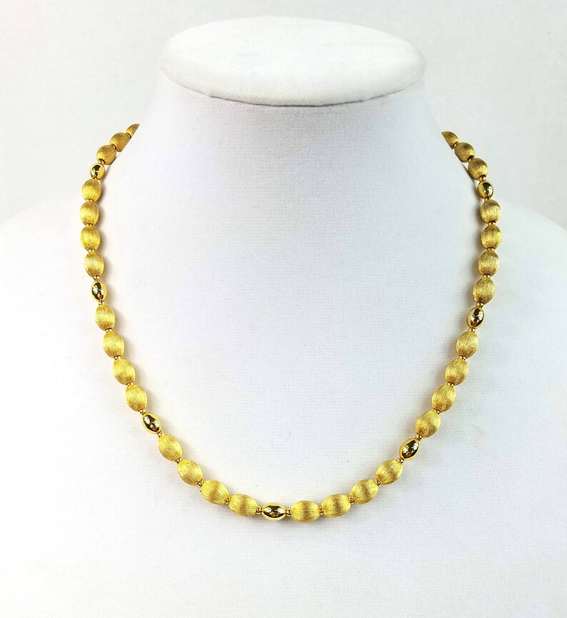 Op de afbeelding: Een gouden ketting met ovale kralen. De kralen hebben een getextureerd oppervlak.