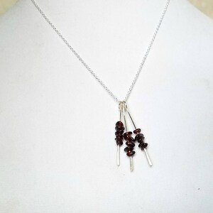 May include: A silver chain necklace with a pendant featuring four strands of small, dark red garnet stones.