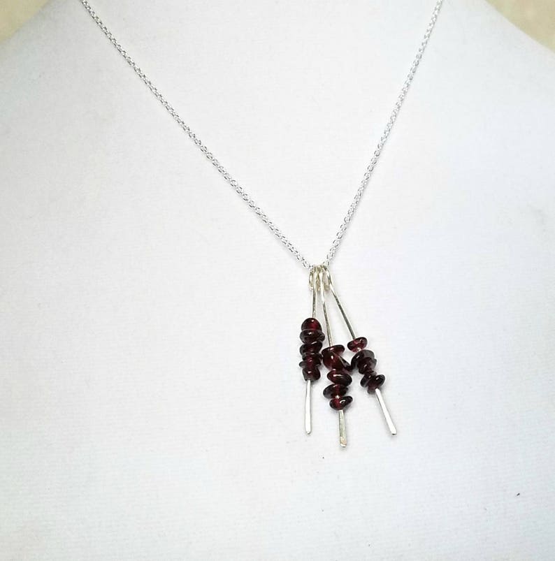 May include: A silver chain necklace with a pendant featuring four strands of small, dark red garnet stones.
