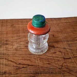 Puede incluir: Un frasco de vidrio transparente con una superficie texturizada y una tapa roja y verde. El frasco tiene un cuerpo redondo y una boca ancha.