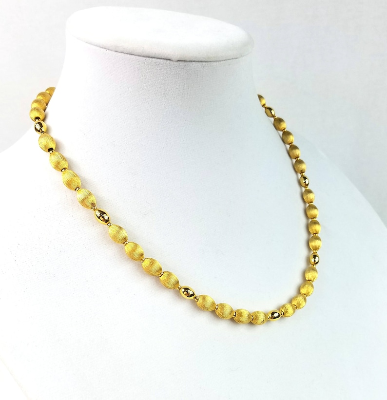 Op de afbeelding: Een gouden ketting met ovale kralen. De kralen hebben een getextureerde, geborstelde afwerking.