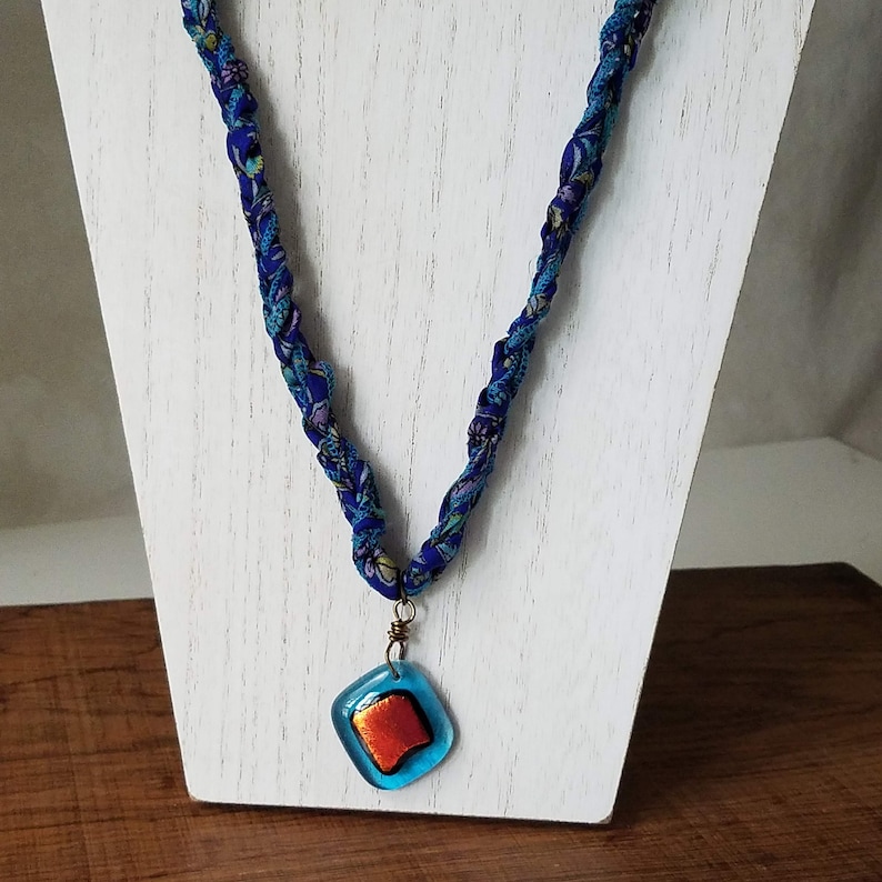 May include: A blue and purple fabric necklace with a blue and orange glass pendant.