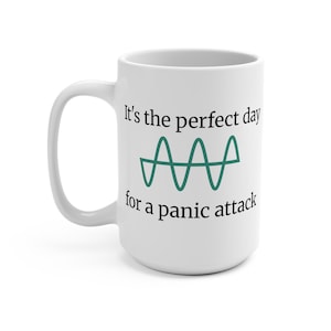 Può includere: Tazza in ceramica bianca con manico curvo. La tazza presenta il testo "It's the perfect day for a panic attack" in nero, con una grafica a onde color verde acqua. La tazza è progettata per le bevande.