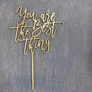 May include: Gold-colored wooden cake topper with the words "You are the best thing" in a cursive font.