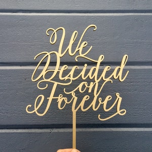 May include: Gold wooden cake topper with the text "We Decided on Forever" in a cursive font.