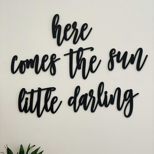 May include: Black wooden wall decor with the text "here comes the sun little darling" in a cursive font.