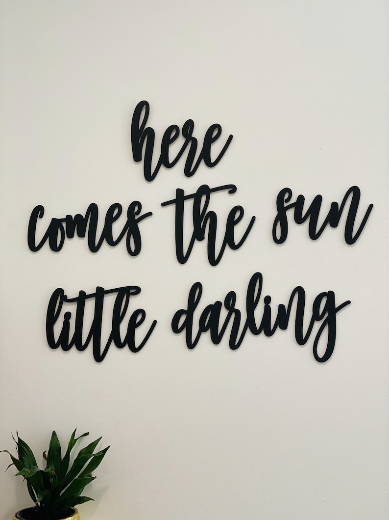 May include: Black wooden wall decor with the text "here comes the sun little darling" in a cursive font.