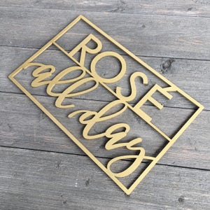 May include: Gold-colored wooden sign with the words "Rose All Day" in a cursive font.