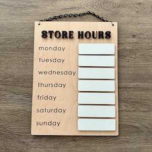 May include: Wooden sign with the text "STORE HOURS" and a list of days of the week: Monday, Tuesday, Wednesday, Thursday, Friday, Saturday, Sunday. Each day has a blank white space next to it for writing in store hours.