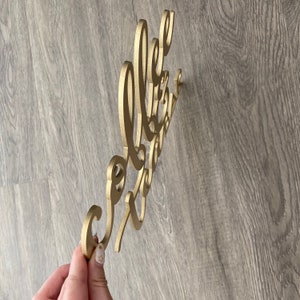 May include: Gold-colored wooden sign with the words "Hello Gorgeous" in a cursive font.