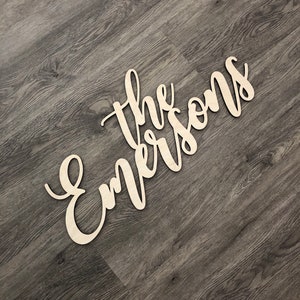 May include: A wooden sign with the name 'The Emersons' in cursive lettering, painted in a light brown colour.