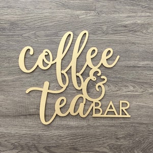 May include: Wooden sign with the words "coffee & tea bar" in a cursive font. The sign is painted gold and has a rustic look.