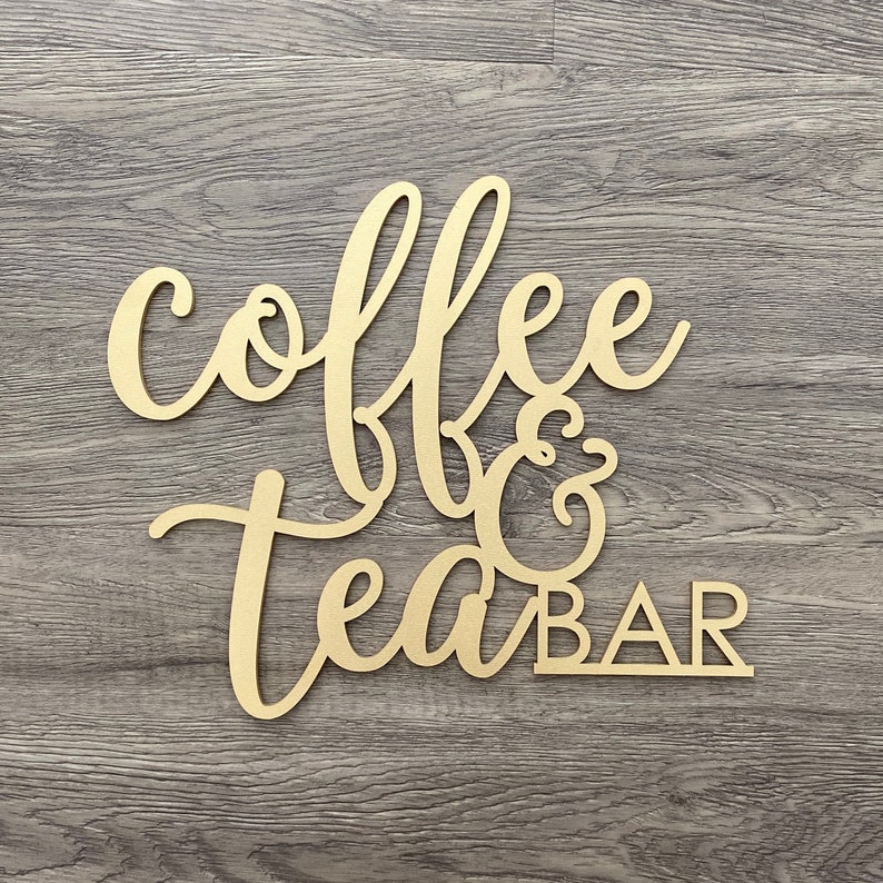 May include: Wooden sign with the words "coffee & tea bar" in a cursive font. The sign is painted gold and has a rustic look.