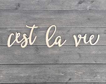 May include: Wooden letters spelling out the French phrase "c'est la vie" on a gray wood background.