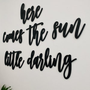 May include: Black wooden wall decor with the text "here comes the sun little darling" in a cursive font.