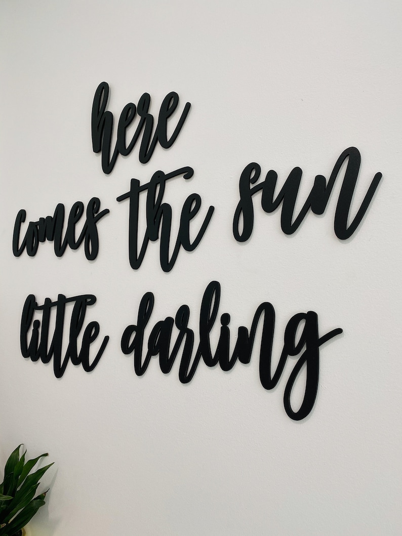 May include: Black wooden wall decor with the text "here comes the sun little darling" in a cursive font.