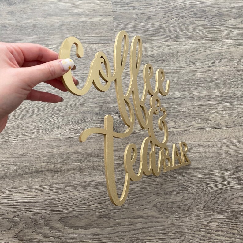 May include: Gold-colored wooden sign with the words "Coffee & Tea Bar" in a cursive font.