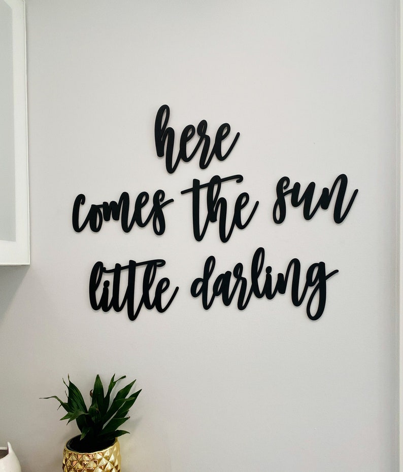 May include: Black wooden wall decor with the words "here comes the sun little darling" in a cursive font.