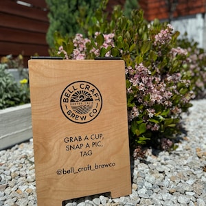 May include: A wooden sign with a black logo that says "Bell Craft Brew Co. Exeter, Calif." and the text "Grab a cup, snap a pic, tag @bell_craft_brewco".